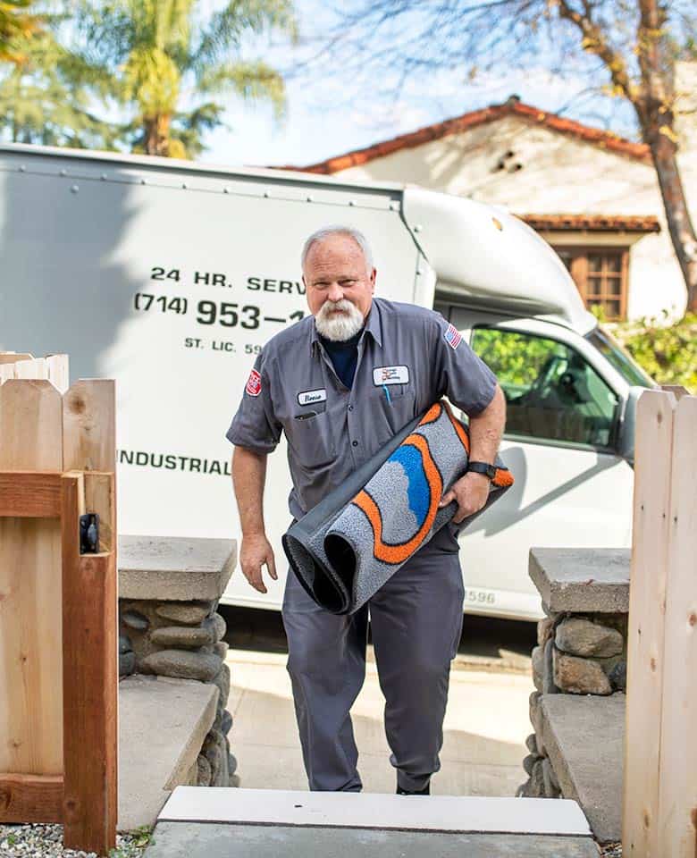 friendly plumber walking up home steps with a service mat in hand